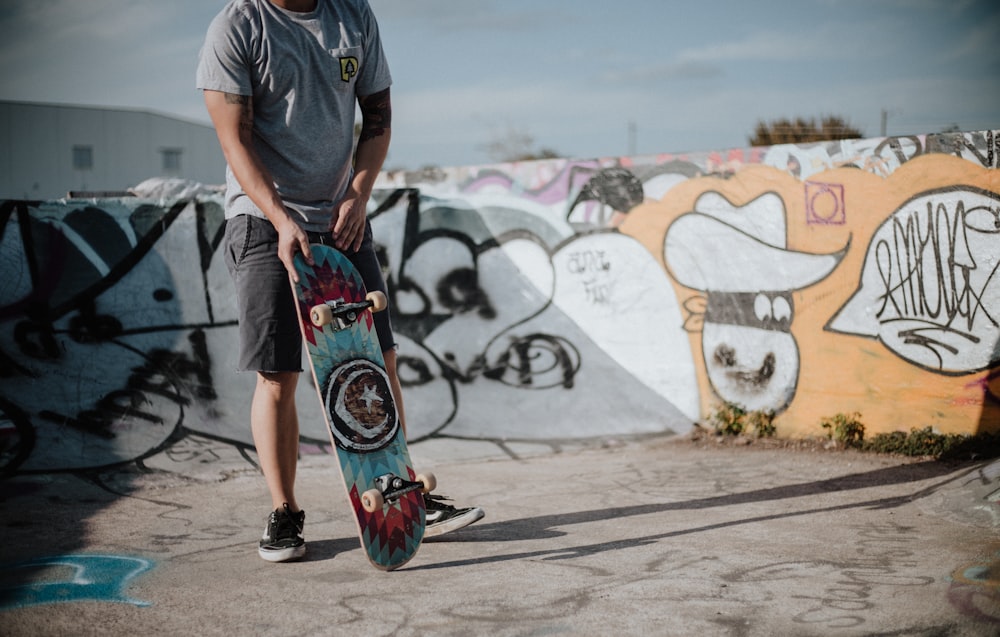man holding teal and red skateboard