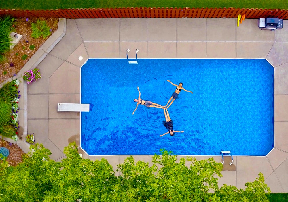 Photographie aérienne de trois femmes flottant sur une piscine formant une hélice