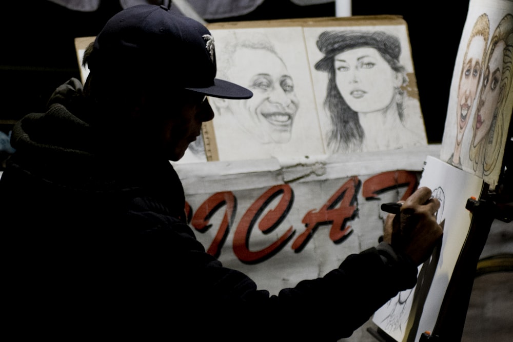 man wearing cap sitting while doing portrait sketches