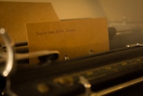 A close-up of an old-fashioned typewriter with a sheet of paper inserted. The paper contains the typed phrase 'People Come First Always.' The scene is dimly lit, with a warm, nostalgic tone enhanced by the contrast between the typewriter and the paper.