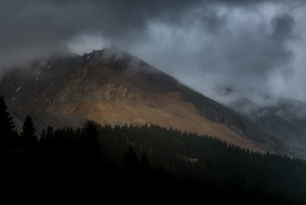 mountain range near forest under cloudy skies