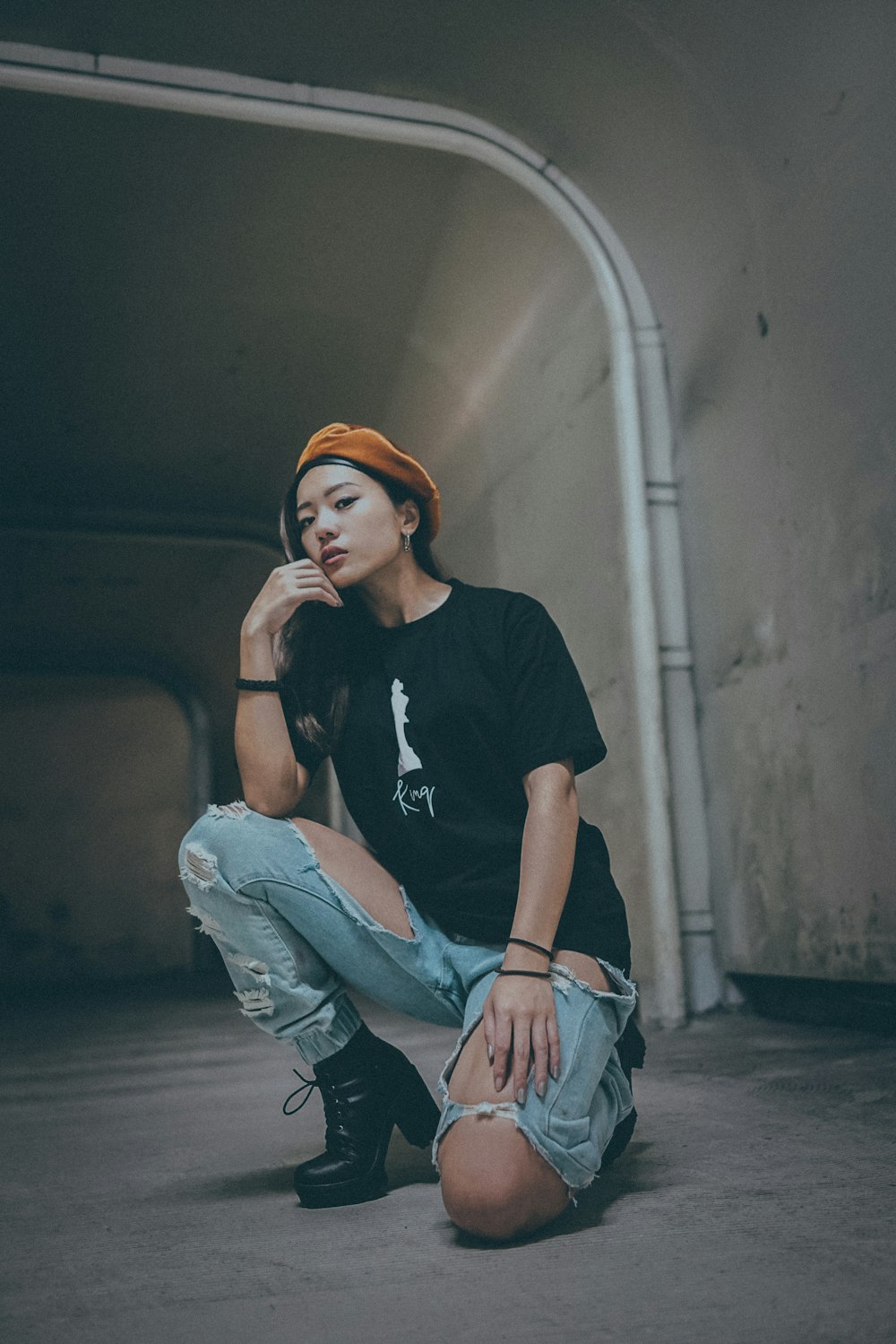 Mujer con camisa negra y jeans de mezclilla azul posando cerca de la pared