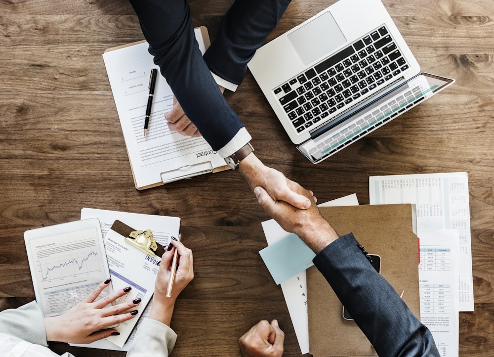 two people handshaking above table with laptop