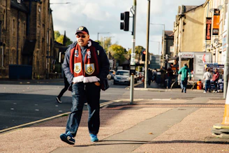 A confident guy walking down a city street wearing slim-fit trousers and a modern jacket, with a red scarf adding a pop of color.