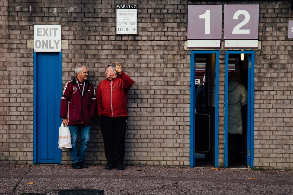 a couple of men standing next to a brick building