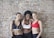 three women taking photo near brown concrete brick wall