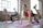Three women are engaged in a fitness routine, following a workout in a bright, spacious studio with large windows. Each woman is on a pink exercise mat, performing a leg lift exercise, focusing on balance and strength.