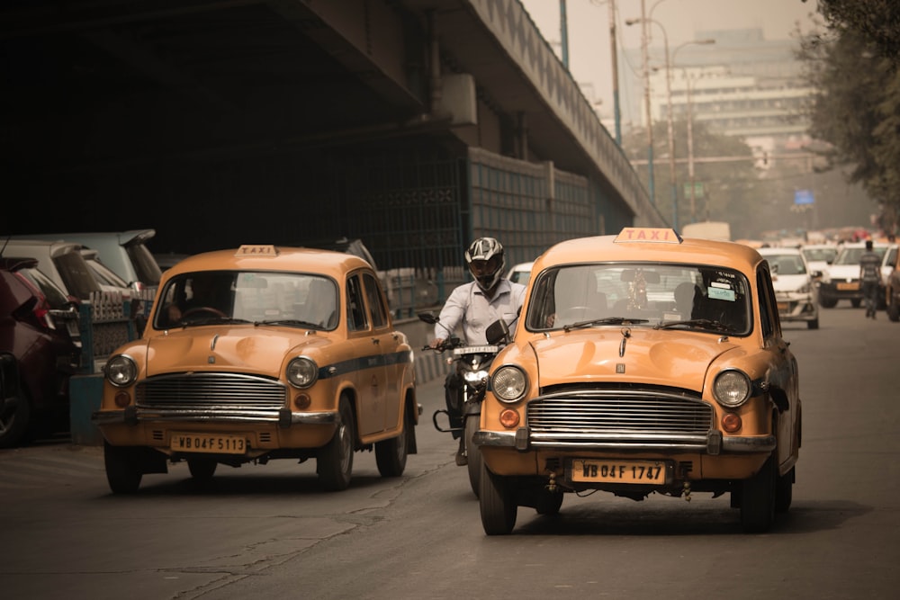 person riding motorcycle in between of two yellow taxi vehicle