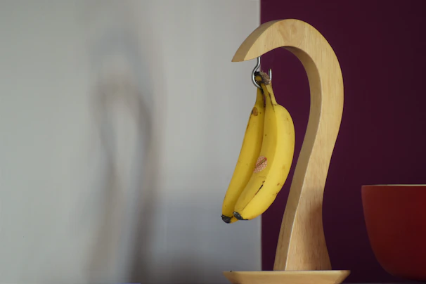 Elegant banana hanger made from smooth, polished wood holding a bunch of ripe bananas.