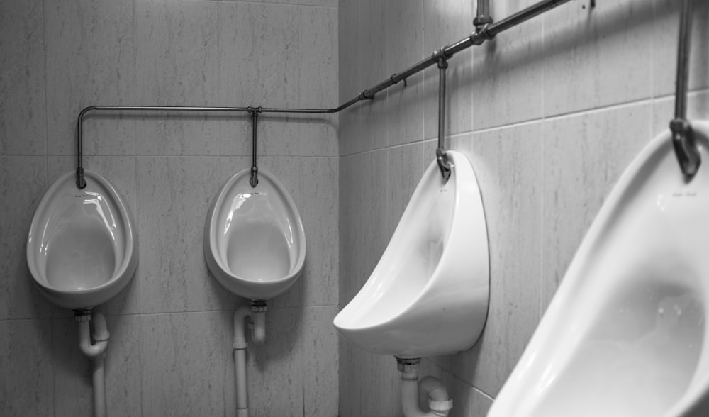 grayscale photography of four white ceramic urinal sinks