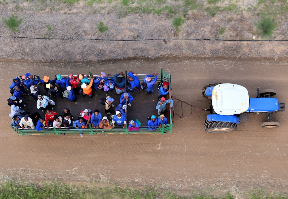 Menschen, die auf einem Lastwagen fahren, der von einem blauen Traktor getragen wird, in der Draufsicht Fotografie