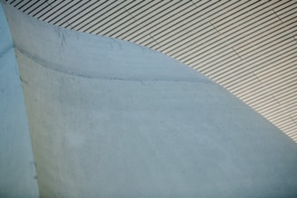 A close-up view of a concrete structure with a smooth, curved surface. The background features a ceiling with parallel lines, creating a geometric pattern.