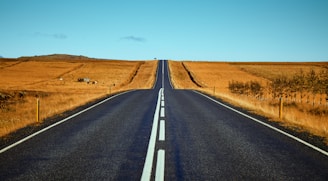 black asphalt road between brown fields during daytime