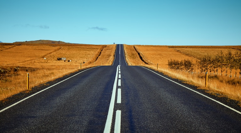 black asphalt road between brown fields during daytime