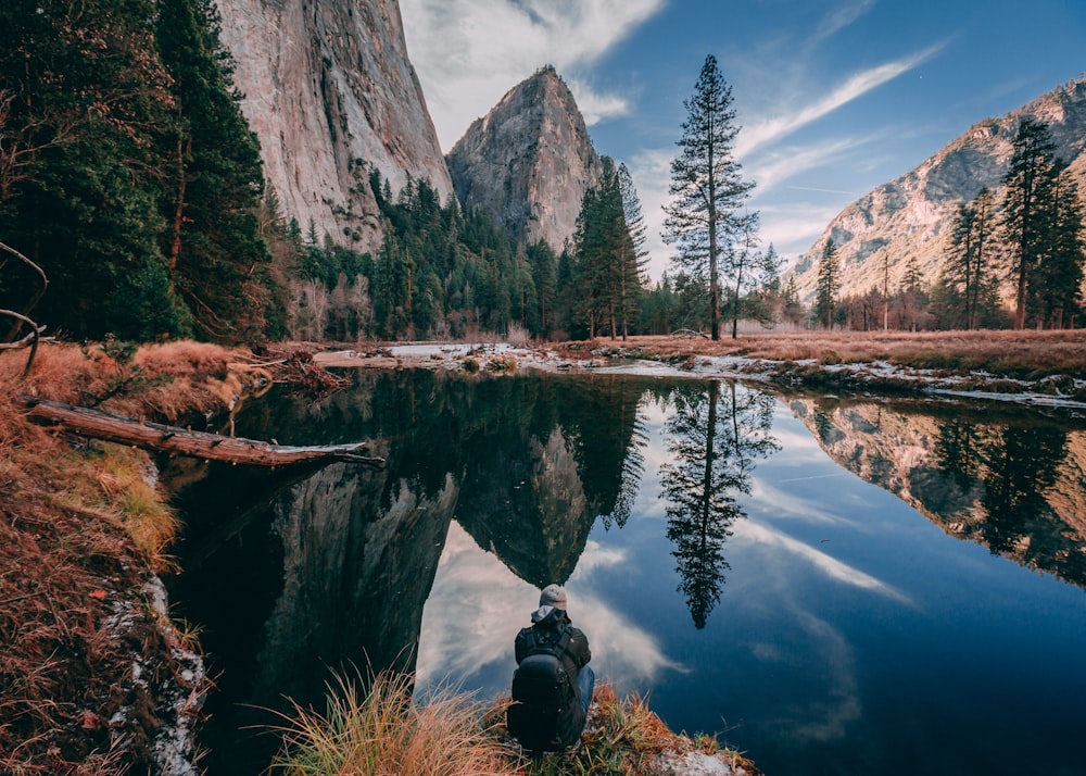 person sitting on rock looking at body of water near forest during daytime