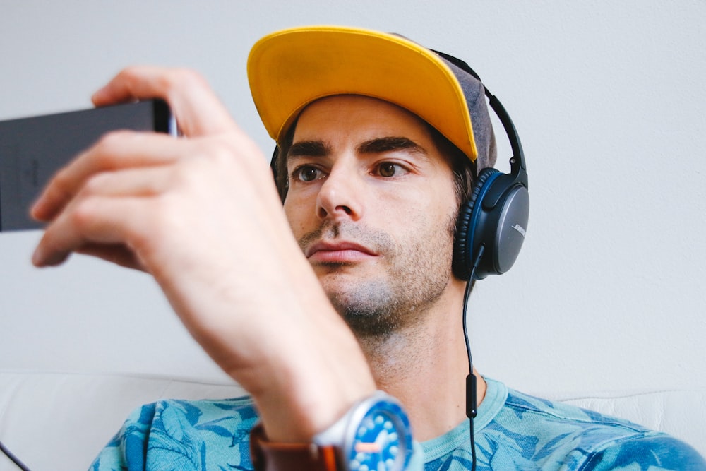 man wearing black corded headphones while holding phone