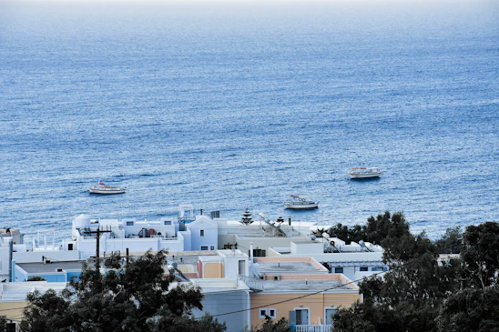 A serene coastal scene showing a group engaged in a lively outdoor workshop near the Mediterranean, with sailboats and lush greenery in the background.