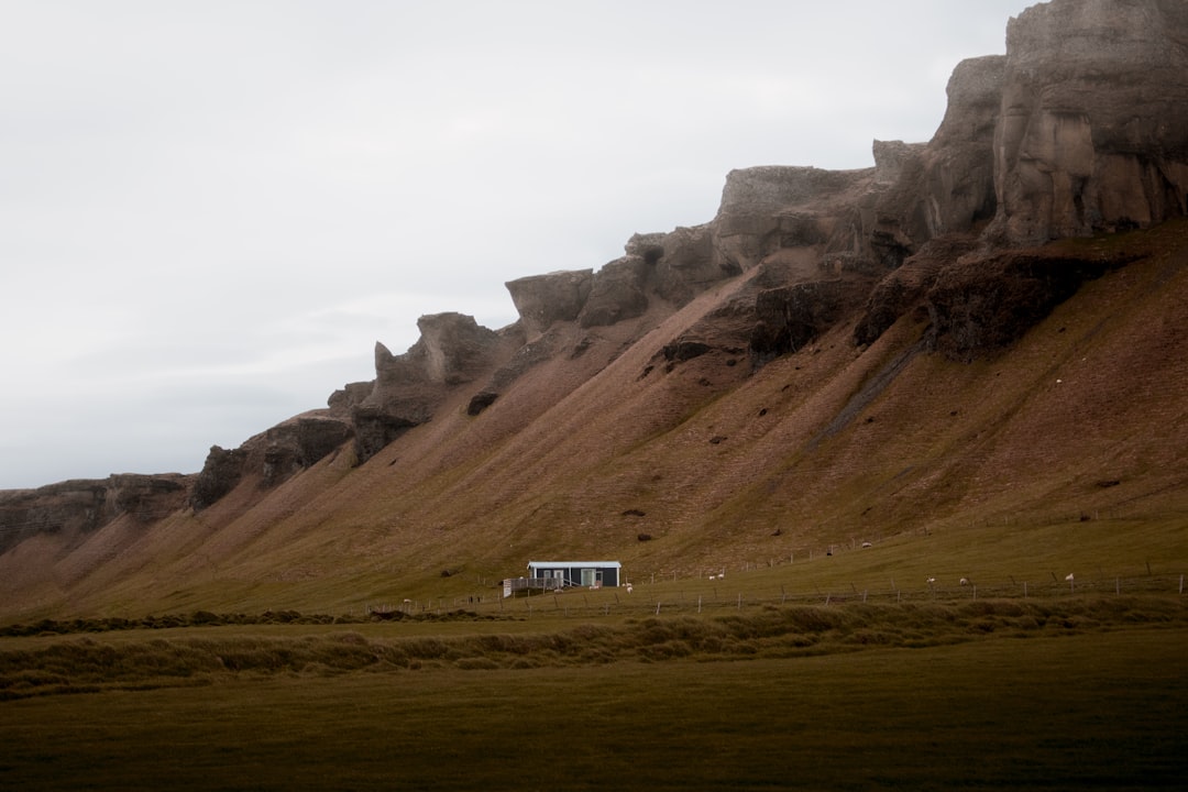 white and blue house on green grass field near brown mountain under white clouds during daytime