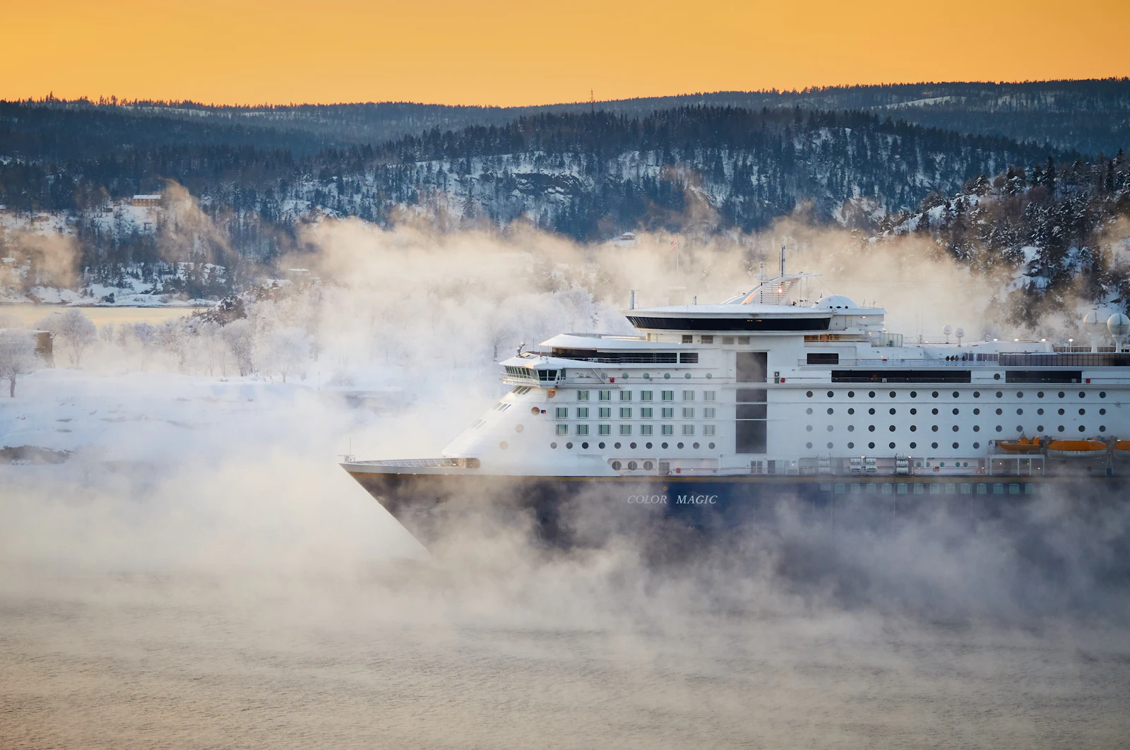Cruise ship sailing through a Norwegian fjord below steep mountains