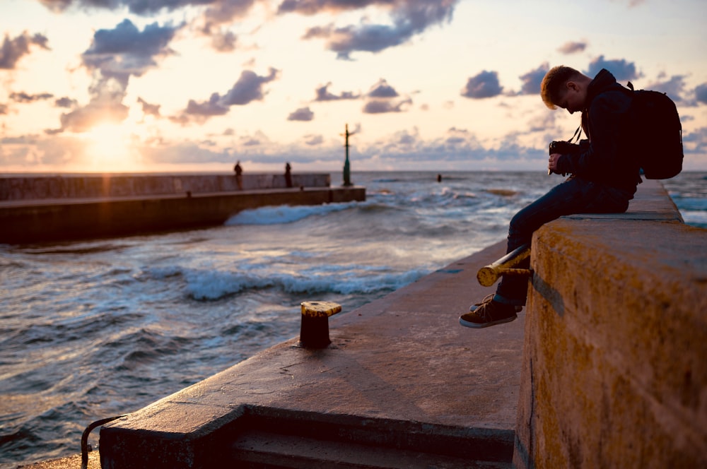 man sitting in front of canal while looking at his camera