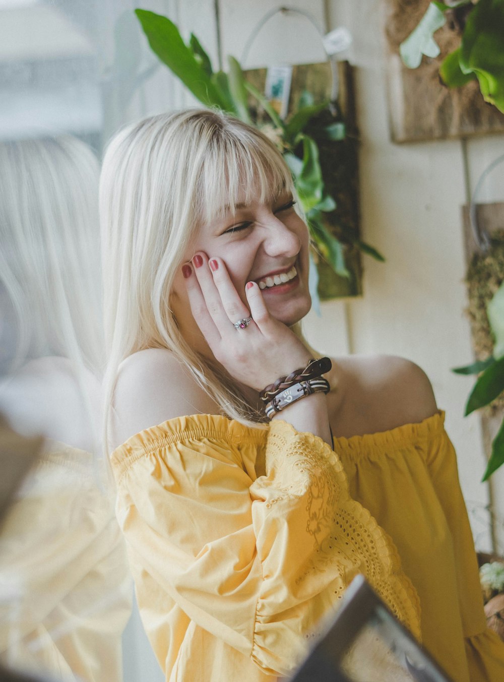 smiling woman in yellow off-shoulder top holding her cheek