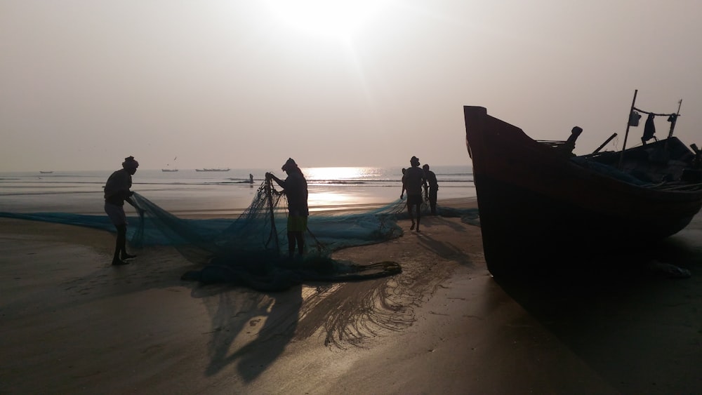 silhouette photography of two person holding fish net near boat at seashore
