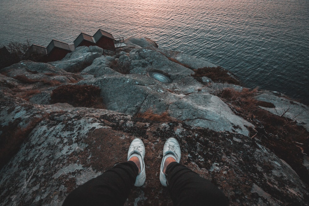 person sitting on rock formation looking at body of water during daytime