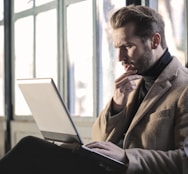 man holding his chin facing laptop computer