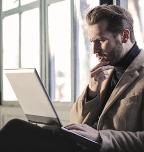 man holding his chin facing laptop computer