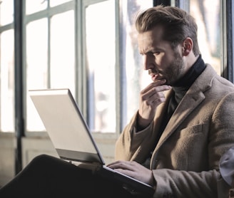 man holding his chin facing laptop computer