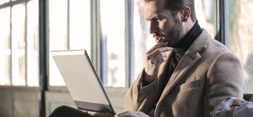 man holding his chin facing laptop computer