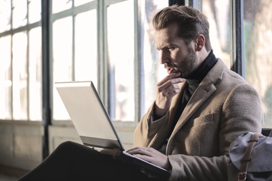 A focused man sitting in a dimly lit room, thoughtfully taking an online test on his laptop.