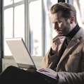 man holding his chin facing laptop computer