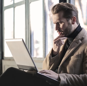 man holding his chin facing laptop computer