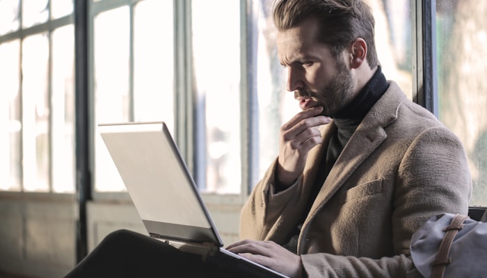 man holding his chin facing laptop computer