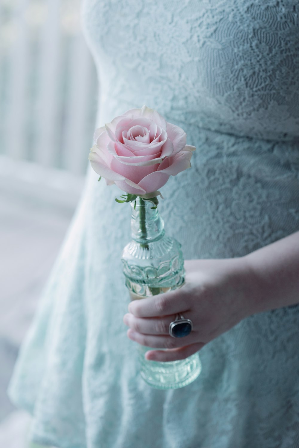 Persona che tiene il fiore rosa in bottiglia di vetro