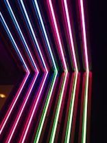 Vertical neon lights in vibrant colors arranged on a dark background. The lights are mostly pink, blue, and green, creating a striking contrast.