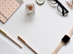 flat lay photo of gold Apple Watch, clear eyeglasses and pens
