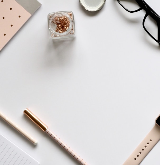 flat lay photo of gold Apple Watch, clear eyeglasses and pens