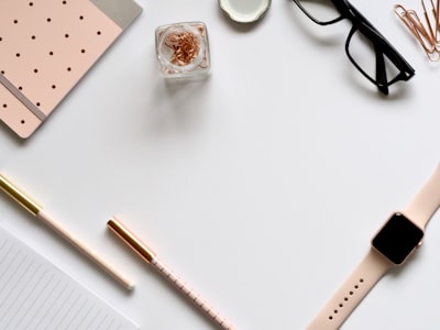 flat lay photo of gold apple watch, clear eyeglasses and pens desk teams background