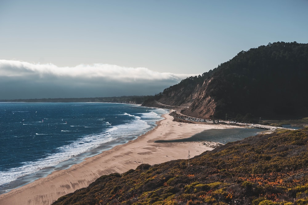 photo of seashore near green mountain