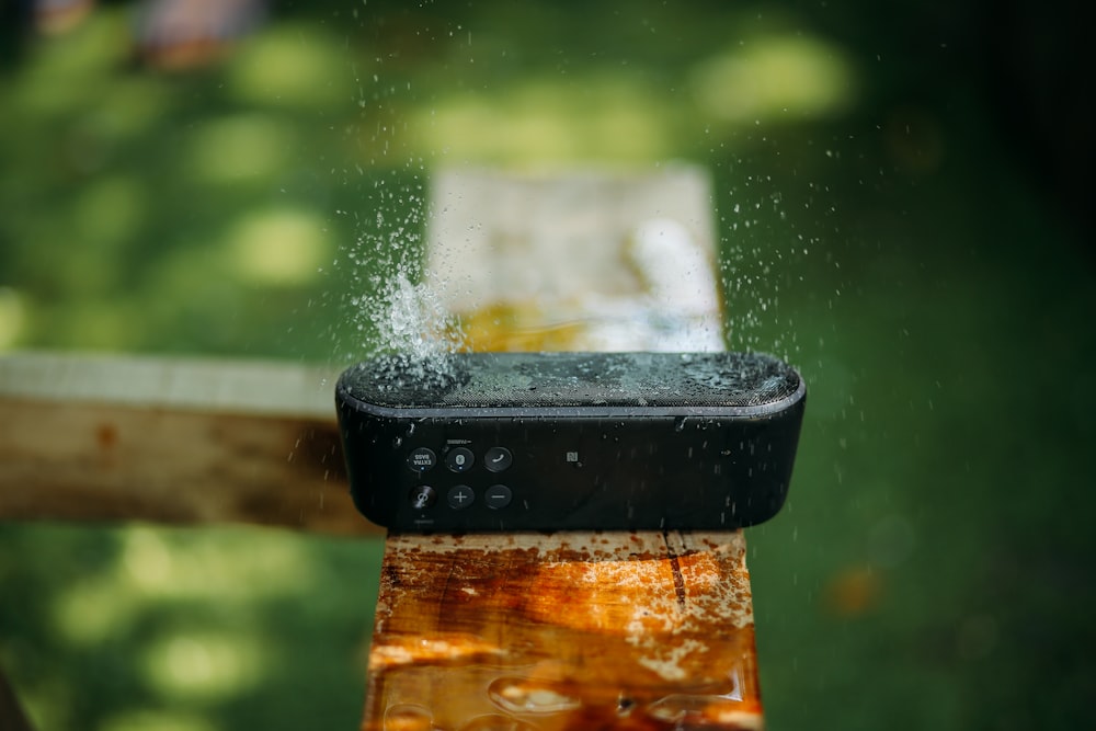 selektive Fokusfotografie eines wasserfesten, länglichen schwarzen tragbaren Bluetooth-Lautsprechers auf braunem Holz
