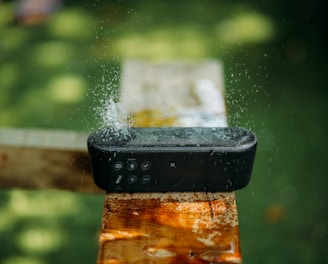 selective focus photography of water resistant oblong black portable Bluetooth speaker on brown lumber