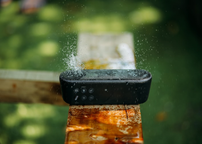 selective focus photography of water resistant oblong black portable Bluetooth speaker on brown lumber