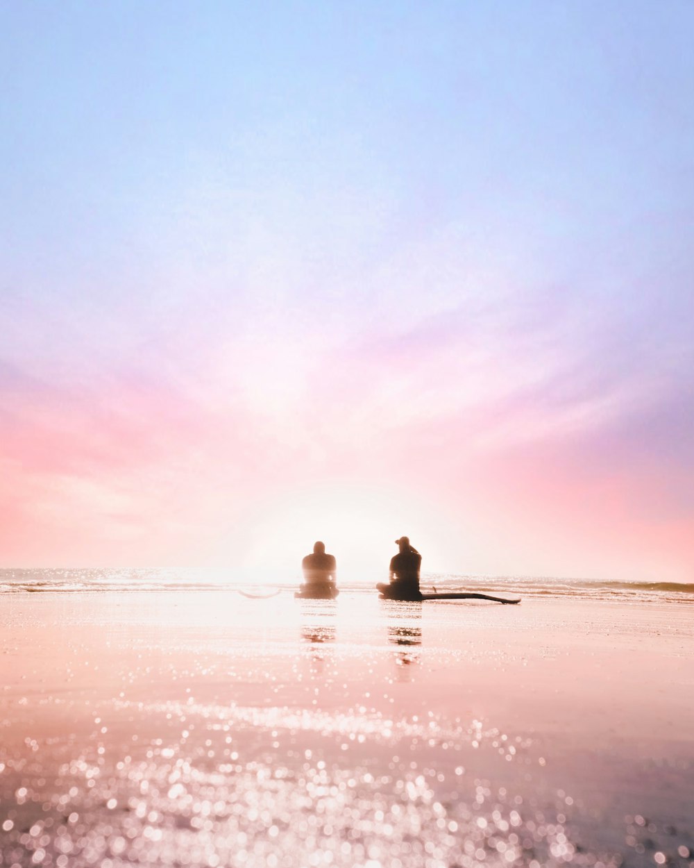 Silhouette von zwei Personen, die in der Morgendämmerung am Meeresufer sitzen