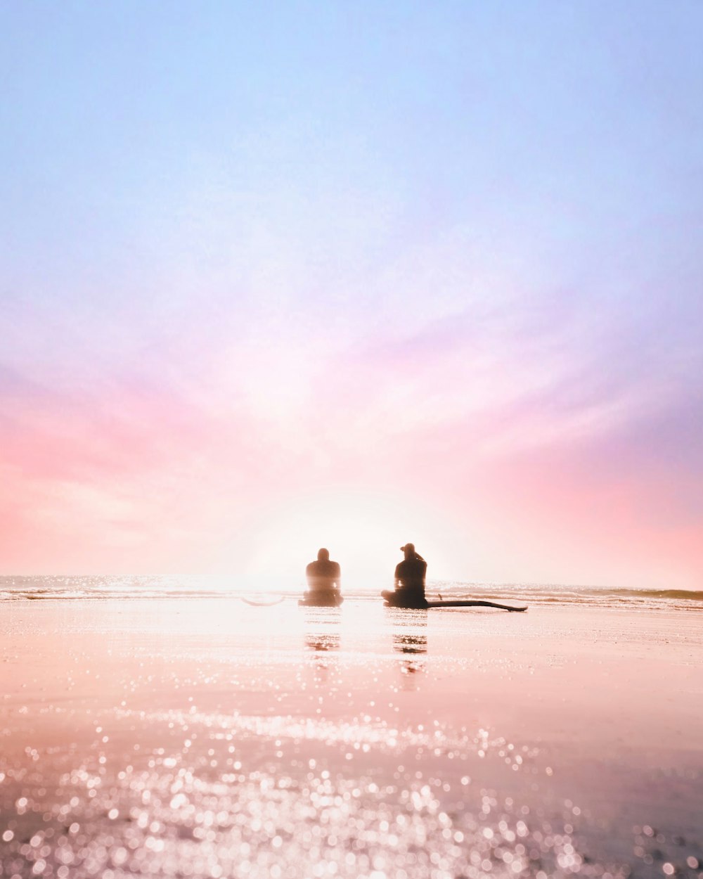 silhouette of two person sitting on seashore during dawn