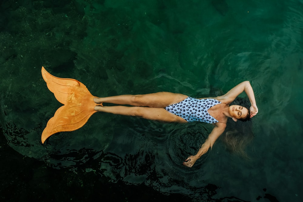 Foto einer Frau, die mit Meerjungfrauen-Schwanzflossen auf einem Gewässer treibt