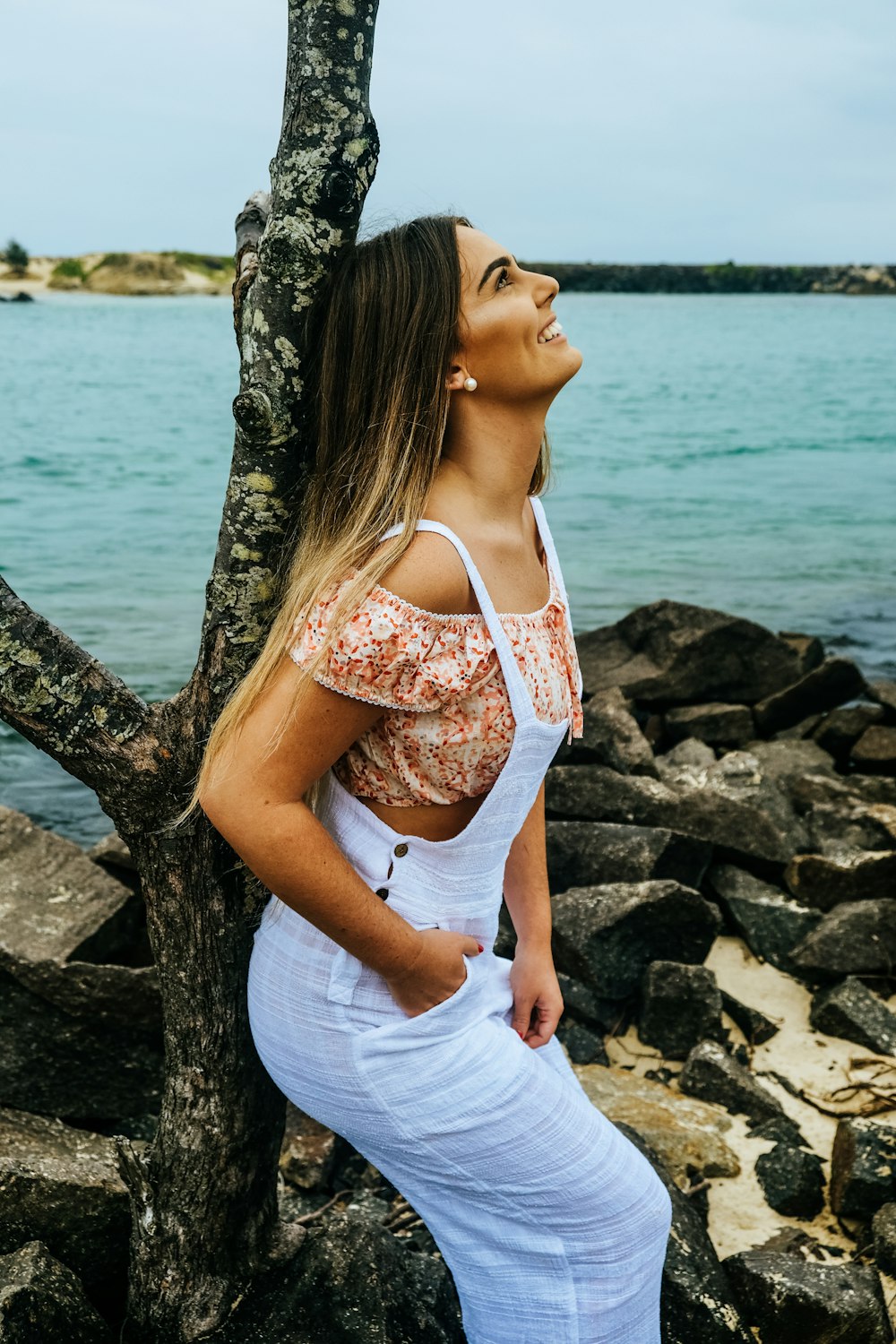 woman leaning on tree with hands in right pocket