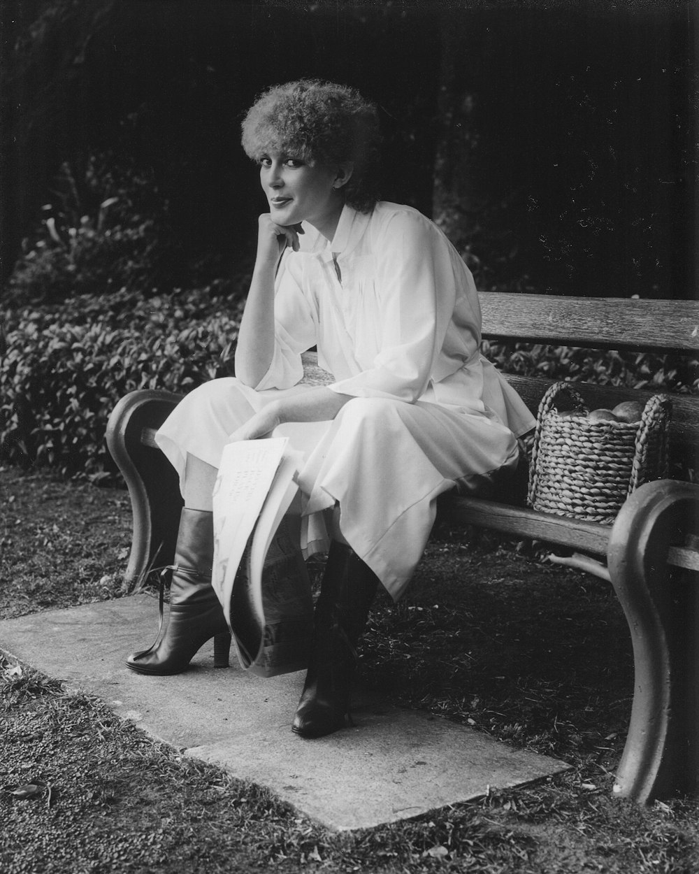 grayscale photo of woman sitting on bench beside basket