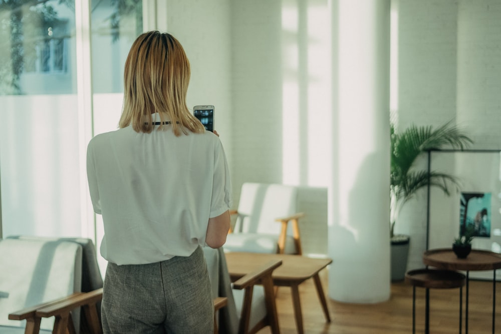 woman standing near white chair using smartphone